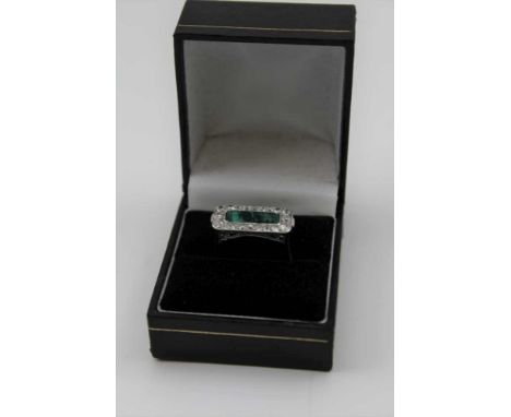 AN ART DECO DESIGN EMERALD AND DIAMOND RING, the cushion cut emerald surrounded by a border of brilliant cut diamonds, white 