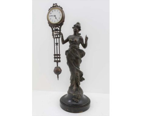 A CONTINENTAL TABLE CLOCK IN THE FORM OF A BRONZED SPELTER WOMAN, in classical costume holding the movement in her right hand