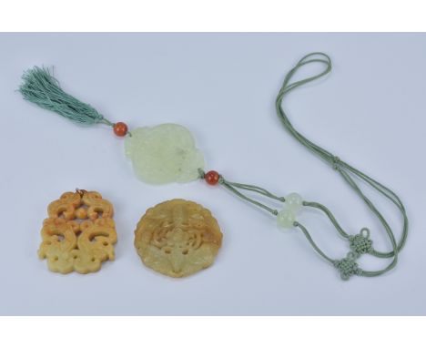 A green jade pendant carved with a deer attached to green string and tassel together with two brown and yellow jade pendants.