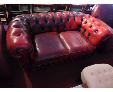 A red leather Chesterfield two seater sofa, raised on castorsH-64cm, W-162cm, D-79cm