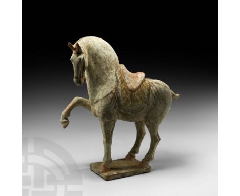 Tang Dynasty, 618-907 AD. A ceramic horse modelled in the round prancing on a rectangular base, right leg raised, moulded sad