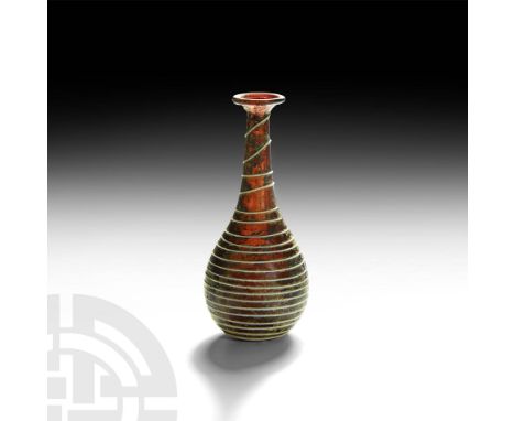 1st century AD. A piriform aubergine glass vase with tapering cylindrical neck, flared rim and rolled lip, embellished with a