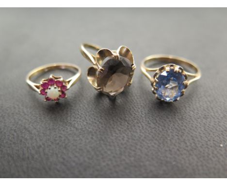 Three 9ct gold dress rings - To include an opal and ruby cluster - A smokey quartz single-stone - Together with a synthetic s