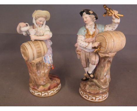 A pair of Meissen late 19th century figures of a gentleman Vintner standing beside a barrel balanced on a tree stump with com