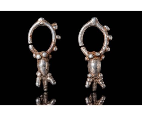 Ca. 1200 - 900 BC.A pair of silver earrings, each with a round-section hoop featuring a slit opening. Along the outer edge of
