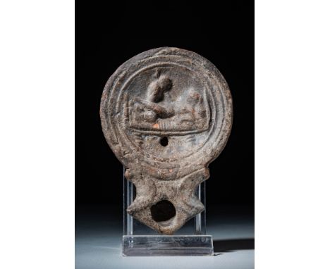 Ca. AD 1 - 300.A mould-made ceramic oil lamp with a circular body and a sunken tondo, surrounded by concentric grooves. The c