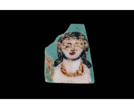 Ca. 100 BC - AD 100. A mosaic glass inlay depicting the bust of a woman against a turquoise ground. The face is rendered in o
