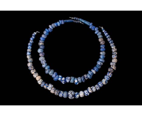 Ca. 370 - 30 BC. A collection of two strings of glass eye beads, composed of predominantly blue annular and spherical shapes.