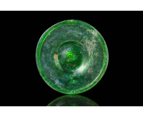Ca. AD 300 - 400. A green glass dish with a broad, shallow body and a recessed centre. The wide, flat rim is well-defined, wi