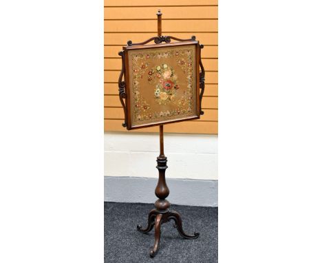 A VICTORIAN MAHOGANY POLE-SCREEN on shaped and curved tripod support and with a floral tapestry panel in a scrolled frame