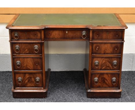 A MAHOGANY BREAKFRONT WRITING DESK with tooled green leather surface and an arrangement of nine drawers, 114cms wide (all lio