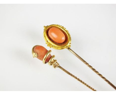 Two coral set stick pins, one designed as an oval coral bead mounted within yellow metal decorative border, the other designe