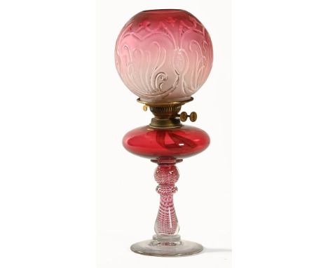 A Victorian oil lamp, with cranberry and white glass spiralled stem, with cranberry reservoir and shade.  Height 48 cm.There 