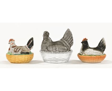 Three hen on nest egg cruets, one ware and another glass and one glass with metal top.  Largest length 14 cm, height 14 cm.Th