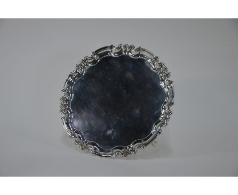 A&nbsp; circular silver salver in the Georgian manner, with shaped and moulded pie-crust rim, on scroll feet, William Hutton 