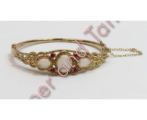 A 9 carat gold hinged bangle, set with three opals and four small ruby points, inner diameter approximately 5.5cm, 16.8 g gro