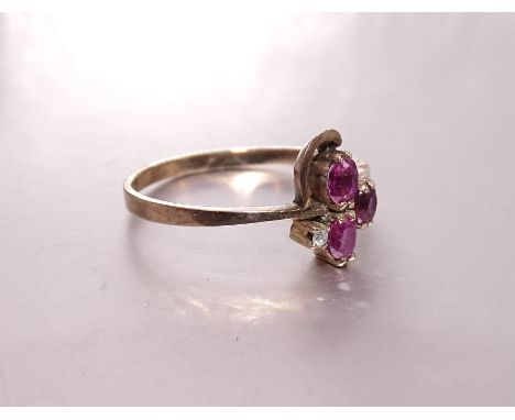 A ruby and diamond ring of asymmetric design set three oval rubies and one brilliant-cut diamond, in unmarked yellow metal mo