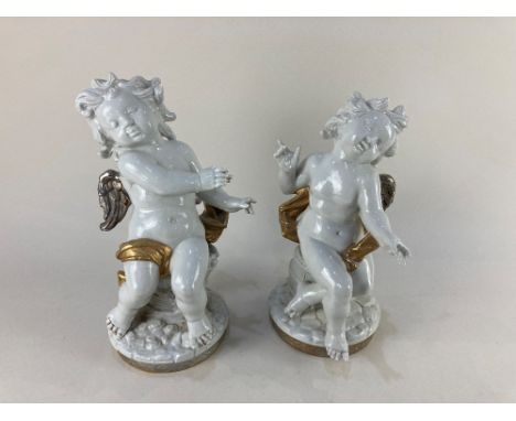 A pair of modern white ceramic cherubs with silver coloured wings, one seated on a barrel. the other on a basket of grapes, p