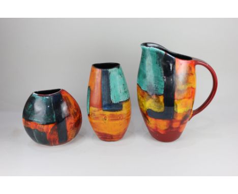 A large Poole pottery jug, with abstract decoration in blue, green and orange, on red ground, 32cm high, together with two Po