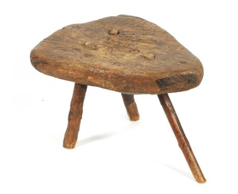 AN EARLY PRIMITIVE ELM STOOL with a thick-cut triangular top; raised on stick legs.43cm wide 36cm deep 28cm high