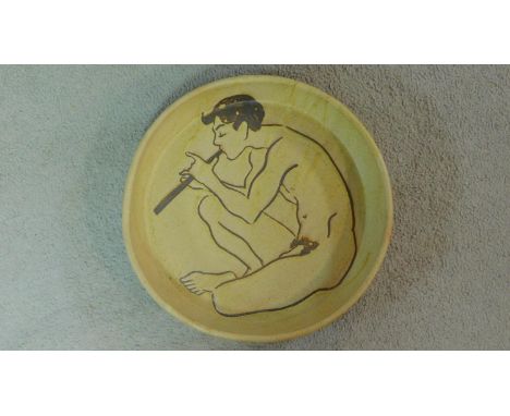 A mid century cream glazed studio pottery Sgraffito bowl by London artist Lucy Rickards, depicting a seated male figure playi