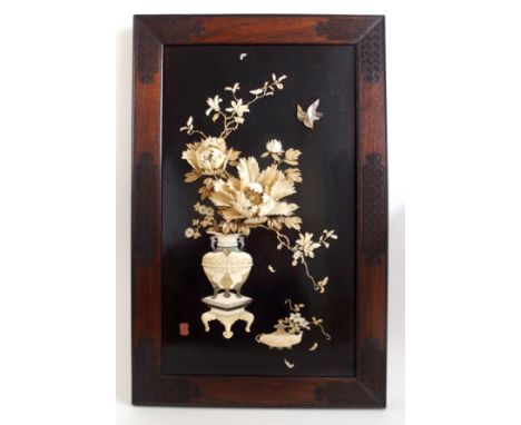 A Japanese lacquered wall plaque onlaid with flowers issuing from an urn standing on a pedestal with a lamp beside, in bone, 