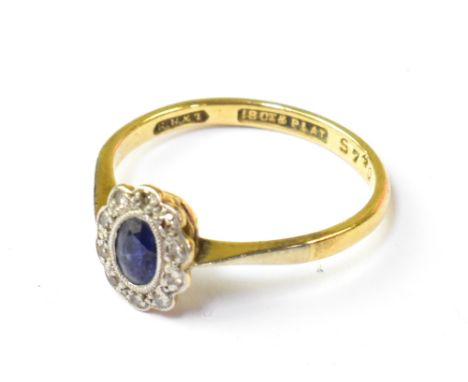 An 18ct yellow gold ring with central bezel sapphire within a flowerhead border of ten tiny diamonds, in platinum mount, size