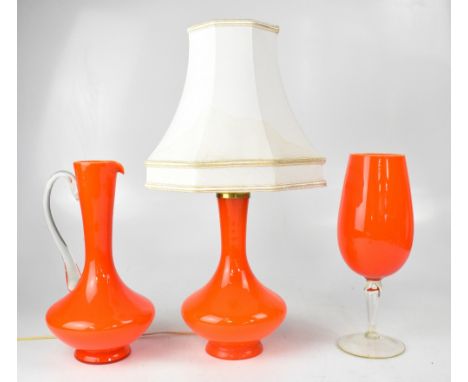 Three pieces of retro orange glassware comprising a baluster-form table lamp, height 25cm, a large decorative wine glass, hei