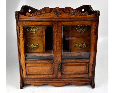 An Edwardian smoker's cabinet with twin glazed and panelled doors enclosing a central well and four short drawers with pipe r