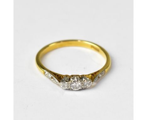 An 18ct gold ring set with central claw set diamond, flanked by two smaller claw set diamonds and three tiny diamonds to the 