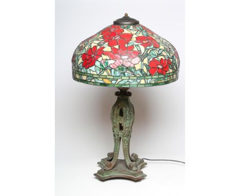 A LARGE TIFFANY STYLE TABLE LAMP, modern, the leaded red floral shade on a verdigris bronzed metal base of moulded pierced ba