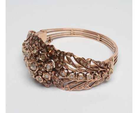 A VICTORIAN DIAMOND BANGLE, the central flower boss collet set with flat cut brown stones within open anthemion shoulders fur