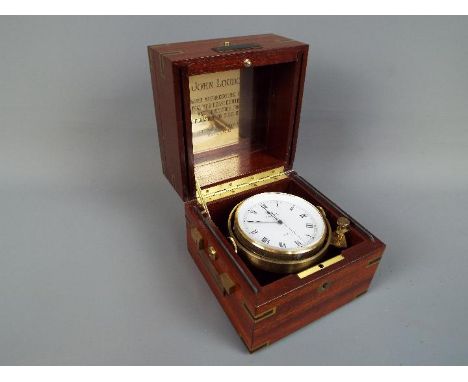 A Relide boxed ships gimbal chronometer. The brass bound mahogany box enclosing brass cased clock with white enamel dial and 