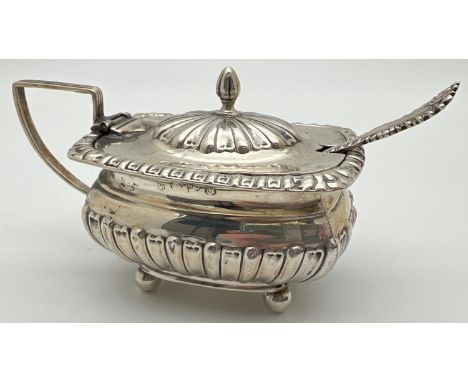 A Victorian silver mustard pot with blue glass liner and silver spoon. Pot raised on 4 ball feet with fluted design body, hin