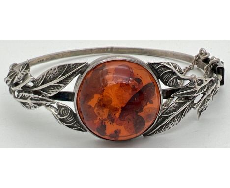 A silver bangle style bracelet set with a round cut piece of cognac amber with leaf design to both sides. Complete with safet