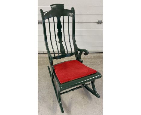 A vintage painted wood rocking chair with spindle back and turned detail. Painted dark green with red velvet upholstered seat