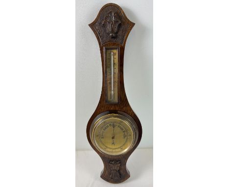 A vintage dark oak cased wall barometer with integral thermometer. Carved foliate design to oak case. Approx. 59cm long. 