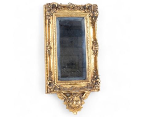 A modern wall hanging mirror, with ornate giltwood and composite frame, with small shelf supported by composite cherub decora