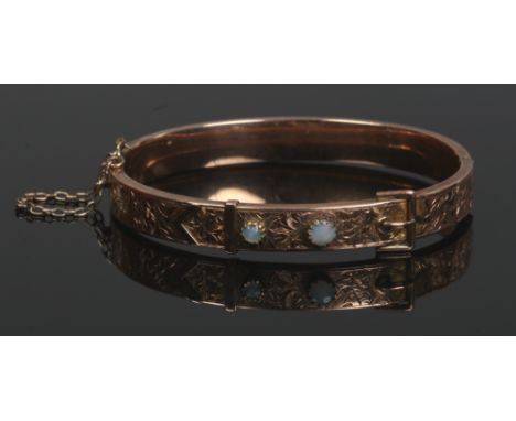 A Victorian 9ct gold bangle. Formed as a belt, chased with scrolling ivy leaves and set with an opal and moonstone, gross wei