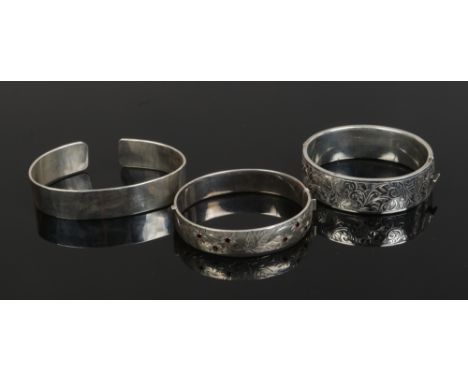 Three silver bangles including two chased examples, one set with garnets, 96 grams.Condition report intended as a guide only.