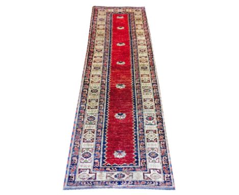 FINE VINTAGE KAZAK RUNNER, 253cm x 76cm, repeat medallions on an abrashed ruby field within multiple geometric borders.