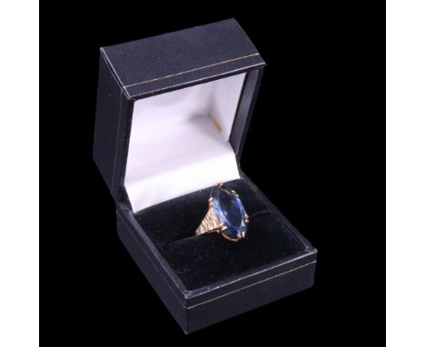 A blue paste and 9 ct yellow metal dress ring, the marquise-cut stone claw-set between tapering, bark-textured shoulders, 19 