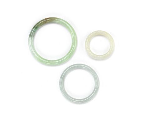 THREE JADE BANGLES19th/20th centuryComprising: a small white jade bangle with C-scroll bands and two jadeite bangles.9.5cm (3