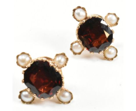 A pair of gold, garnet and pearl stud earrings. The earrings having a central mixed cut garnet set in a decorative mount surr