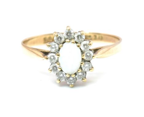A hallmarked 9ct gold CZ and opal cluster ring. The ring set with a central oval opal cabochon surrounded by a halo of round 