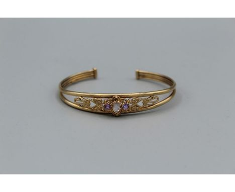 A 9ct gold openwork bangle, set with aquamarine flanked by amethysts. 7gm