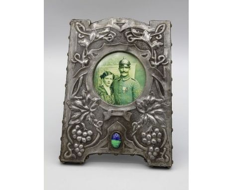 An Art Nouveau pewter photograph frame, with blue /green enamel stone and trailing fruiting vine decoration on oak easel supp