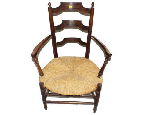 An Arts and Crafts oak and elm Sussex chair with ladder back support with finials to the uprights, carved arm rests, rush sea