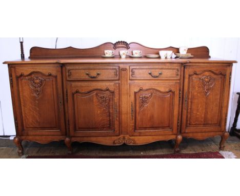 A French early 20th century light oak break front sideboard with carved tray back, moulded top, two central, four cupboards u