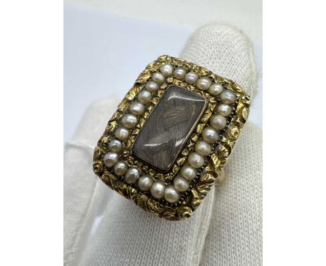 A Decorative Pearl Set Mourning Ring, the antique central glazed hairwork panel within pearl border and outer foliate carved 